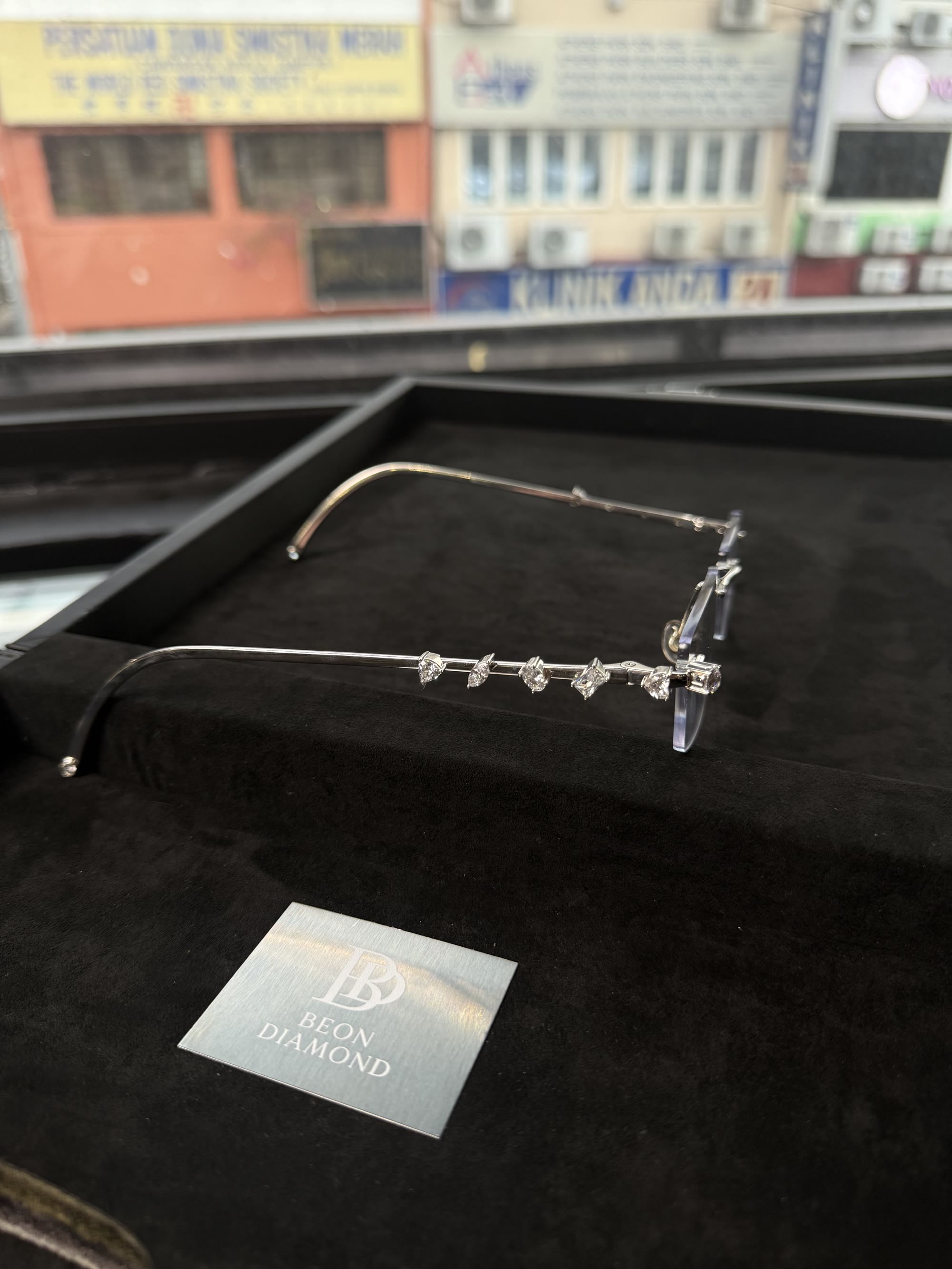 The frame in side profile, six diamond cuts along the temple, Kuala Lumpur shophouses out of focus behind